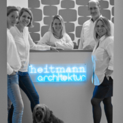 Das Team steht vor dem Empfangstresen, vor dem in Neonschrift "Heitmann Arichtektur" leuchtet.
